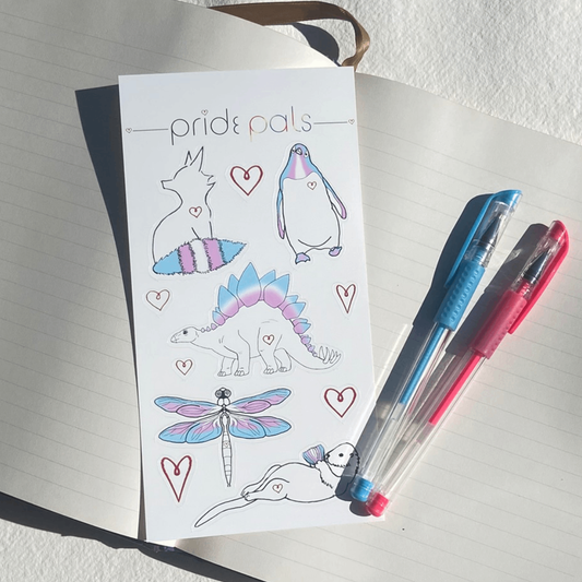 Sheet of vinyl stickers with animal designs and 'pride pals' branding, placed on an open notebook with two pens.